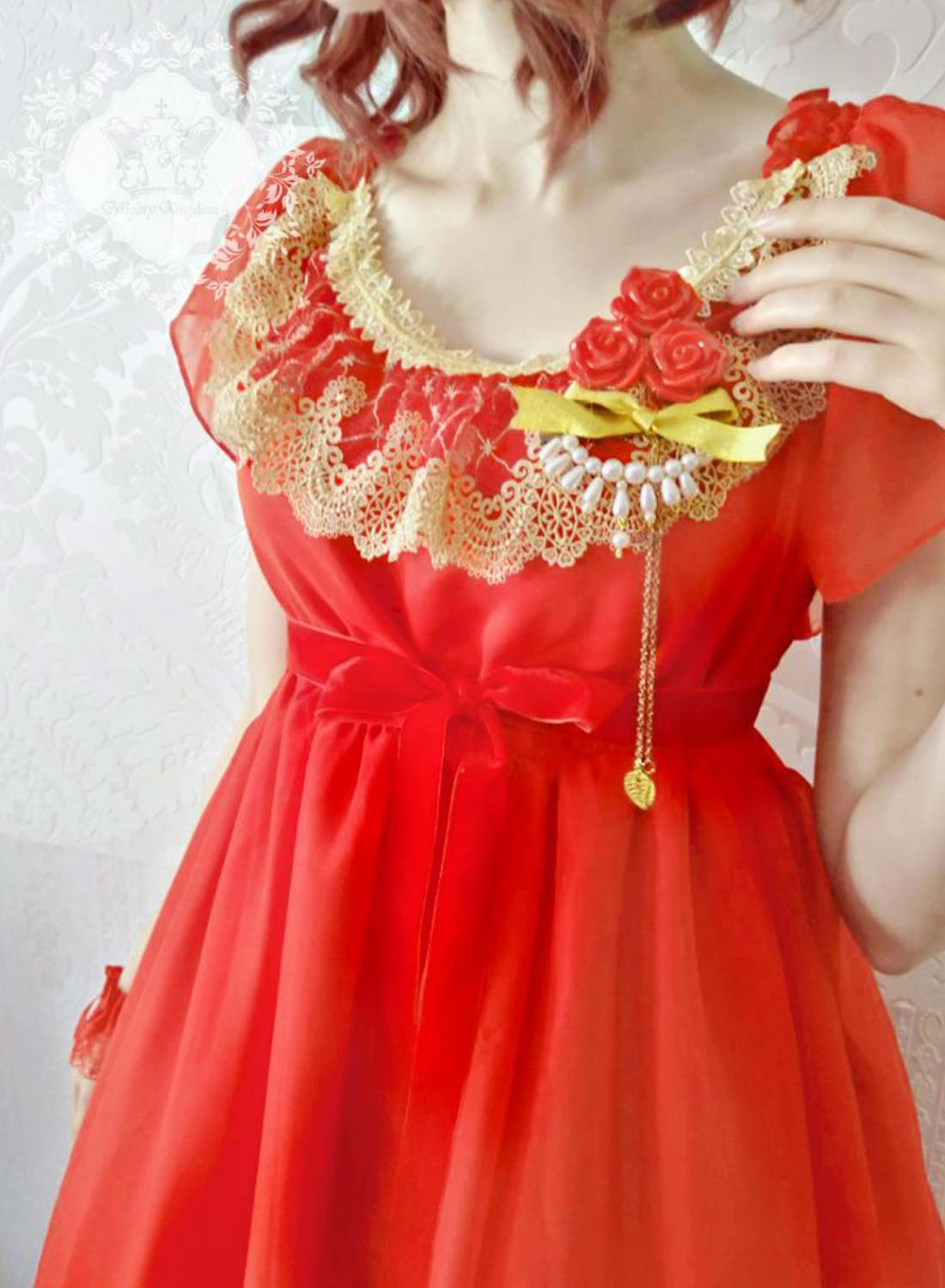 Nahaufnahme eines getragenen rotem Chiffonkleids mit Rosenbrosche und Spitzenkragen